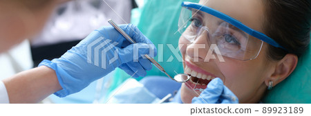 Doctor examining oral cavity of female patient using dental instruments in clinic 89923189