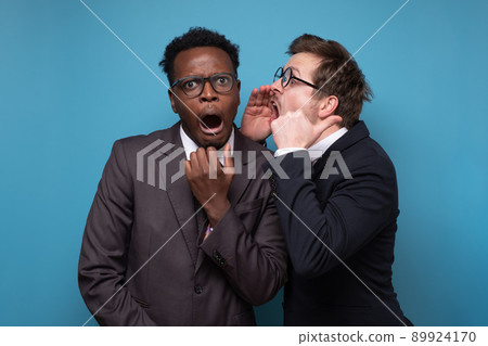 Two shocked young men coworkers whisper gossip and tell secret behind his hand sharing news. 89924170