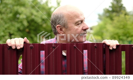 Mature caucasian man carefully watching over the fence. Curious neighbors and private life Mature caucasian man carefully watching over the fence. Curious neighbors and private life 89924349