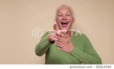 Senior caucasian woman laughing at your funny joke, pointing finger to the camera. 89924498