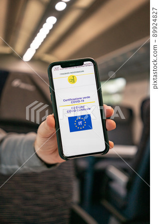 Italian online covid certificate. A man's hand shows a phone screen with a vaccination certificate against the background of the train cabin 89924827