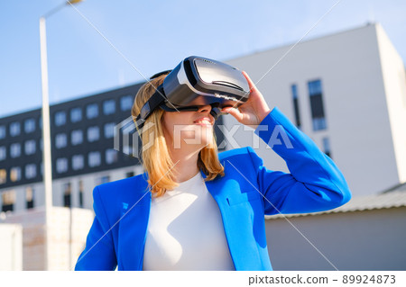 Smiling woman in vr glasses experiencing augmented reality in front of a business center. Futuristic future in the metaverse world. Smiling woman in vr glasses experiencing augmented reality in front of a business center. Futuristic future in the metaverse world. 89924873