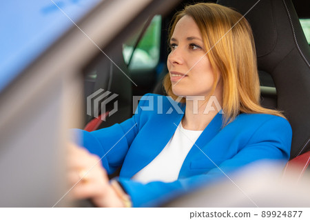 Smiling business woman driving a car in the blue suit Smiling business woman driving a car in the blue suit 89924877