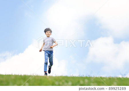 Elementary school boy running in the field against the background of the blue sky 89925289