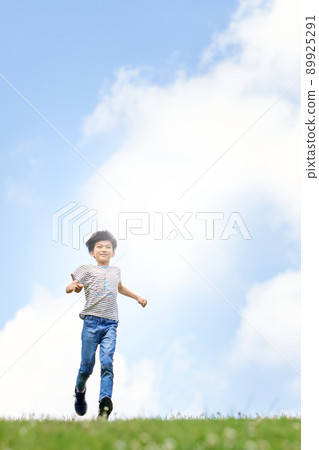 Elementary school boy running in the field against the background of the blue sky 89925291