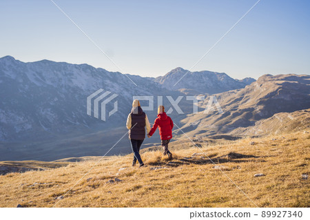 Montenegro. Mom and son tourists in the background of Durmitor National Park. Saddle Pass. Alpine meadows. Mountain landscape. Travel around Montenegro concept Montenegro. Mom and son tourists in the background of Durmitor National Park. Saddle Pass. Alpine meadows. Mountain landscape. Travel around Montenegro concept 89927340