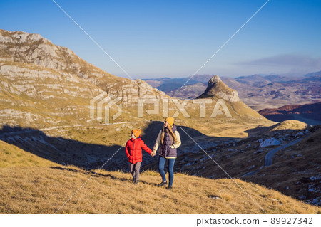 Montenegro. Mom and son tourists in the background of Durmitor National Park. Saddle Pass. Alpine meadows. Mountain landscape. Travel around Montenegro concept Montenegro. Mom and son tourists in the background of Durmitor National Park. Saddle Pass. Alpine meadows. Mountain landscape. Travel around Montenegro concept 89927342