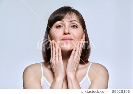 Portrait of middle aged woman looking at camera on light studio background Portrait of middle aged woman looking at camera on light studio background 89928306