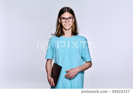 Portrait of positive teenage student guy with glasses with laptop looking at camera, light studio background Portrait of positive teenage student guy with glasses with laptop looking at camera, light studio background 89928337