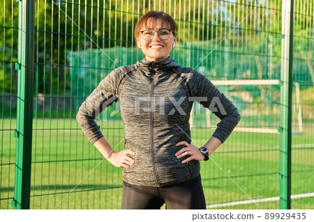 Active sporty mature woman standing in sports stadium, after training, running, exercising Active sporty mature woman standing in sports stadium, after training, running, exercising 89929435