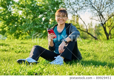 Outdoor portrait of mature smiling woman looking at camera sitting on grass Outdoor portrait of mature smiling woman looking at camera sitting on grass 89929451