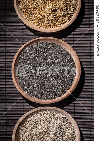 Sesame, chia and flax seeds in wooden dishes, wooden spoon with chia on wooden base. Top view.Vertical format. Sesame, chia and flax seeds in wooden dishes, wooden spoon with chia on wooden base. Top view.Vertical format. 89929480