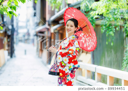 一個穿著和服的年輕女子拿著一把日本雨傘 一個穿著和服的年輕女子拿著一把日本雨傘 89934451