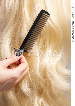 Barber holding comb on long curly blonde hair background closeup Barber holding comb on long curly blonde hair background closeup 89935449