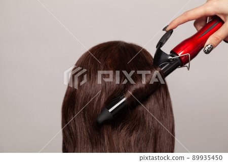Brunette woman curling her hair with curler straightener Brunette woman curling her hair with curler straightener 89935450