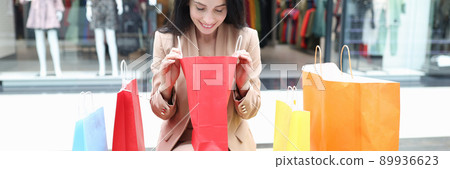 A woman sits in a shopping center and looks into a package A woman sits in a shopping center and looks into a package 89936623