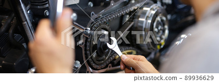 A man spins a part on a motorcycle with a wrench A man spins a part on a motorcycle with a wrench 89936629