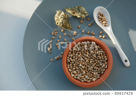 A bunch of cannabis seeds lie on a spoon and plate with several dried buds A bunch of cannabis seeds lie on a spoon and plate with several dried buds 89937429
