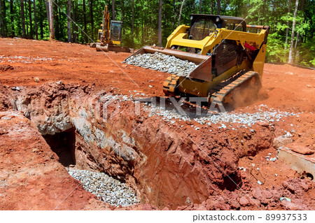 Worksite outdoors with loader small bulldozer moving the gravel breakstone at construction area 89937533
