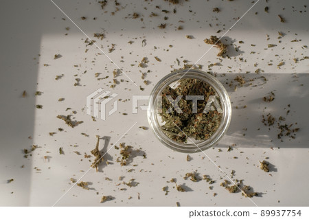 Weed Store. Glass jar with dried cannabis buds on white background with crushed weed. 89937754