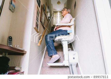 Senior woman using automatic stair lift on a staircase at her home. Medical Stairlift for disabled people and elderly people in the home. Selective focus. 89937811