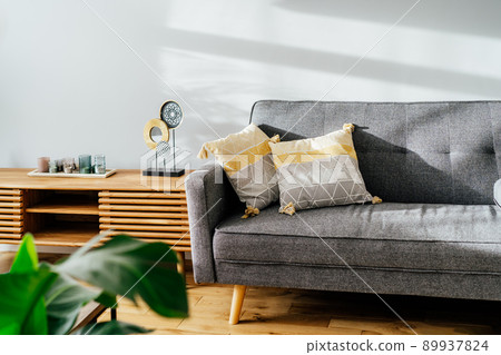 Stylish living room interior with designer console with decor and gray sofa with graphic pillows. White walls, green plants in the pots. Light wooden oak parquet. Modern Scandinavian style interior. 89937824