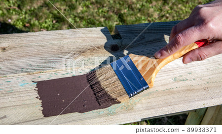 Woman's hand using paintbrush with brown paint. Painted wooden surface 89938371