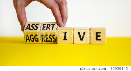 Aggressive or assertive symbol. Businessman turns wooden cubes, changes the word Aggressive to Assertive. Beautiful white background, copy space. Business, psychological aggressive assertive concept. 89939145