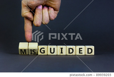 Guided or misguided symbol. Businessman turns wooden cubes and changes the word misguided to guided. Beautiful grey table, grey background, copy space. Business and guided or misguided concept. 89939203
