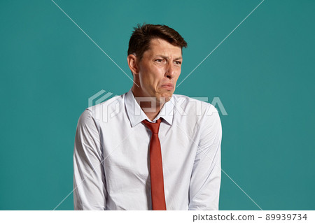Young man in a classic white shirt and red tie posing over a blue background. 89939734