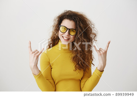 Beautiful funny amazed rocker girl with curly hairstyle and standing with rock sign and looking at camera. studio shot, isolated on grey background 89939949