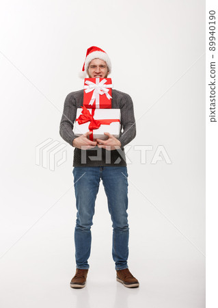 Christmas Concept - young handsome man with beard holding heavy presents with exhausted facial expression on white background. 89940190
