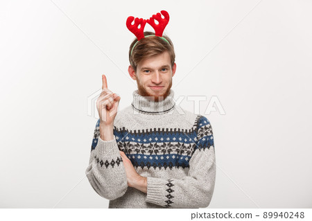 Holiday Concept - Young beard man in sweater enjoy playing and pointing finger upward. Holiday Concept - Young beard man in sweater enjoy playing and pointing finger upward. 89940248
