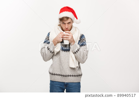 Christmas concept - Young beard man in sweater and santa hat holding a hot coffee cup isolated on white with copy space. 89940517
