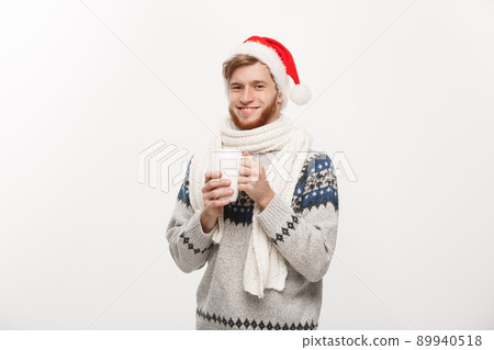 Christmas concept - Young beard man in sweater and santa hat holding a hot coffee cup isolated on white with copy space. 89940518