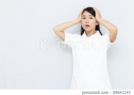 Female nurse in her thirties holding her head Female nurse in her thirties holding her head 89941245