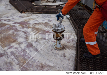 Young offshore engineer sounding fuel oil cargo tank on cargo deck on supply vessel in harbor. 89941278