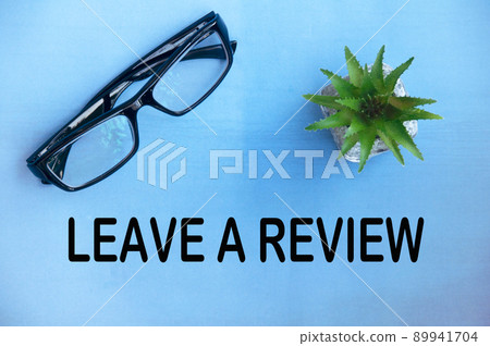Leave a review text on light blue cover with potted plant and glasses background. Feedback concept 89941704