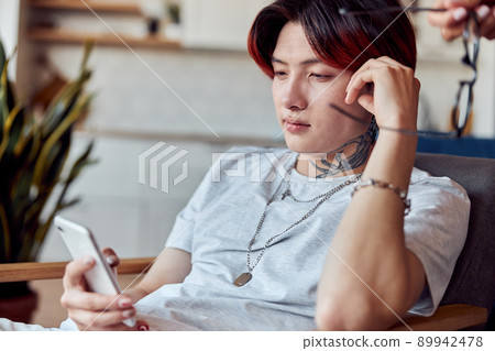 Asian guy sitting at his appartment while using smartphone 89942478
