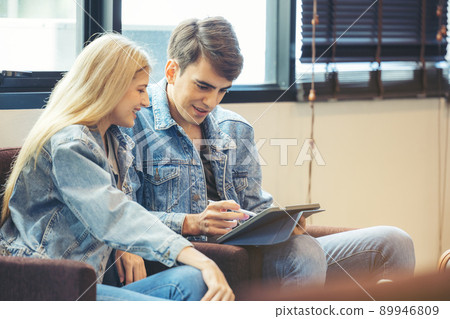 A couple sits in the hotel lobby, looking at a tablet computer. A couple sits in the hotel lobby, looking at a tablet computer. 89946809