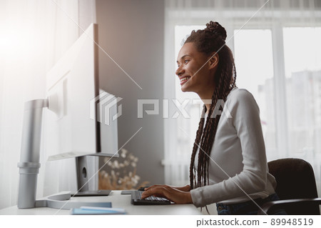 Portrait of cheerful smiled young woman coder working from home browsing on computer Portrait of cheerful smiled young woman coder working from home browsing on computer 89948519