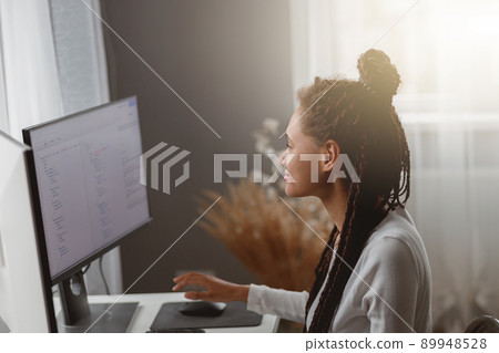 Beautiful mixed-race female coder working on new project texting on computer in apartment Beautiful mixed-race female coder working on new project texting on computer in apartment 89948528