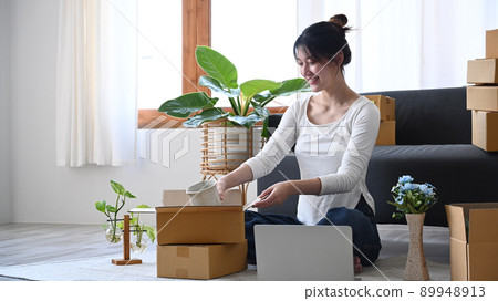 Young woman small business entrepreneur packing product in cardboard box for delivery to customers. Online selling, e-commerce Young woman small business entrepreneur packing product in cardboard box for delivery to customers. Online selling, e-commerce 89948913