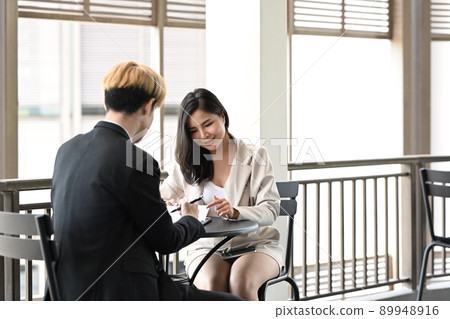Two young business colleagues sitting on a terrace outside office and discussing, sharing startup business plan together 89948916