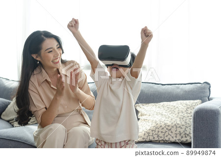 Smiling mother looking son playing games using virtual reality headset(VR) at home. Technology future concept. 89949874