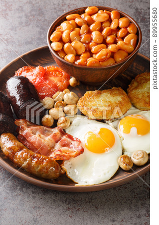 Irish breakfast with fried egg, sausages, black pudding, baked beans, bacon, tomato, hash browns and grilled mushrooms closeup in the plate. Vertical Irish breakfast with fried egg, sausages, black pudding, baked beans, bacon, tomato, hash browns and grilled mushrooms closeup in the plate. Vertical 89955680