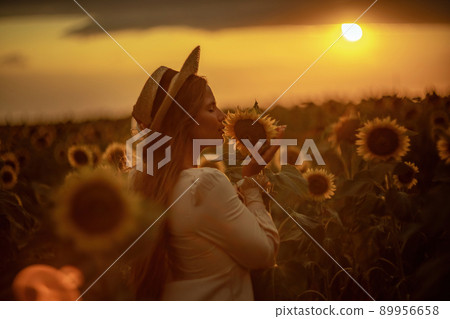 Beautiful middle aged woman looks good in a hat enjoying nature in a field of sunflowers at sunset. Summer. Attractive brunette with long healthy hair. Beautiful middle aged woman looks good in a hat enjoying nature in a field of sunflowers at sunset. Summer. Attractive brunette with long healthy hair. 89956658