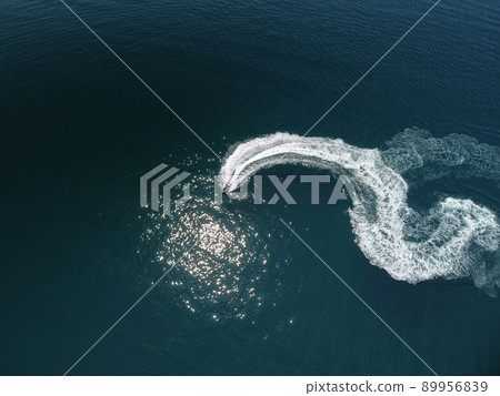 Aerial top down view of water foam trace with nice deep blue shade of ocean. Beautiful white trail on the calm sea surface behind a small powerful motorboat. Propwash. Summer vacation travel concept Aerial top down view of water foam trace with nice deep blue shade of ocean. Beautiful white trail on the calm sea surface behind a small powerful motorboat. Propwash. Summer vacation travel concept 89956839