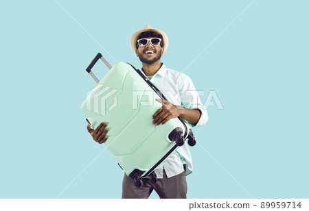 Happy Indian man who is going on holiday trip abroad is holding his suitcase and smiling Happy Indian man who is going on holiday trip abroad is holding his suitcase and smiling 89959714