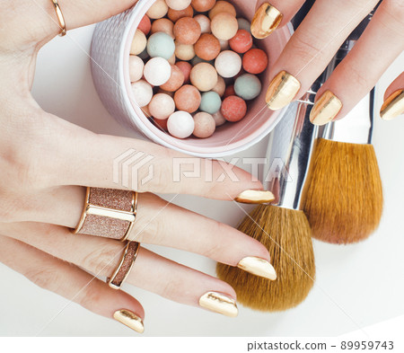 woman hands with golden manicure and many rings holding brushes, cosmetic and rose flower on white background, spa treatment concept close up 89959743